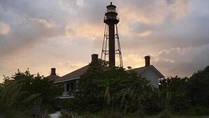 A lighthouse with a metal structure and a white building in the foreground.