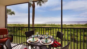 A balcony with a table set for dining, overlooking a beach with a palm tree and ocean view.
