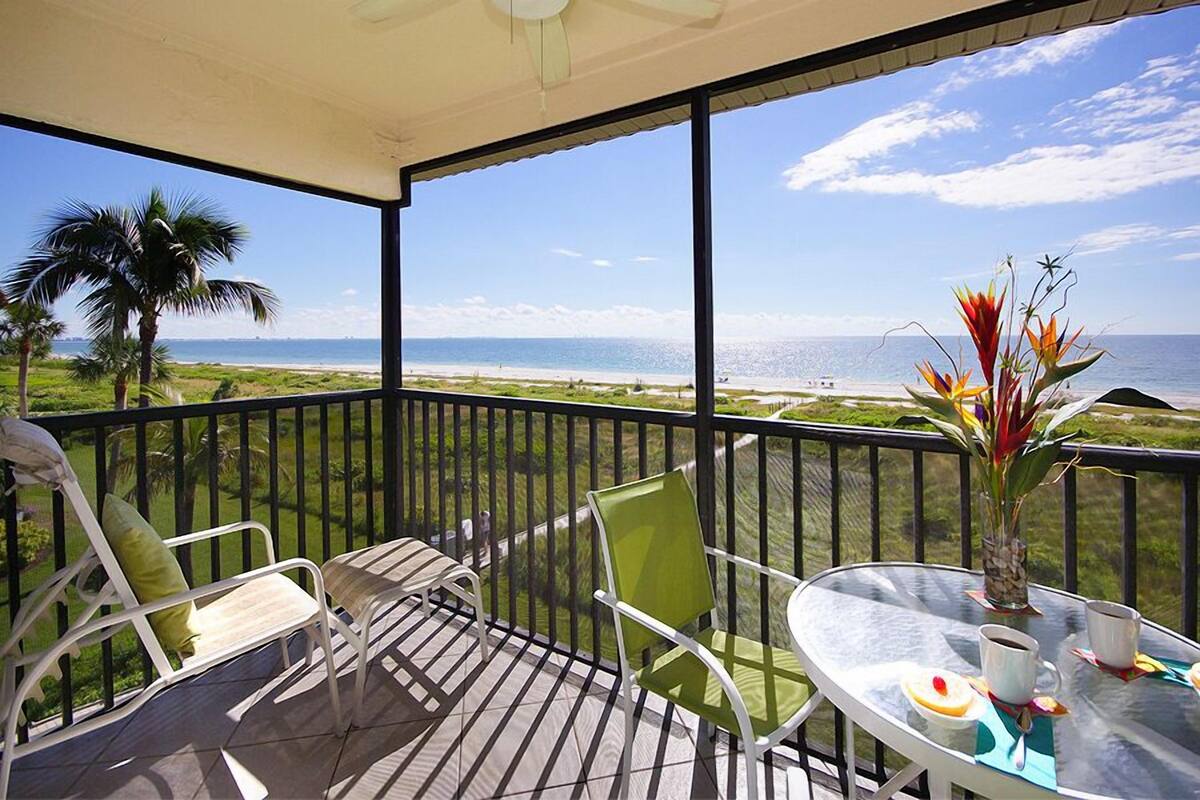 A balcony with a glass table, two chairs, and a vase of flowers.