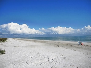 A beach with a clear sky and a few clouds. There is a chair and a red object on the sand.