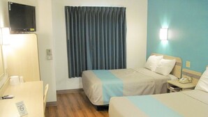 A hotel room with two beds, a desk, a chair, a TV, and a window with curtains. - Motel 6 Avoca, IA (Avoca)