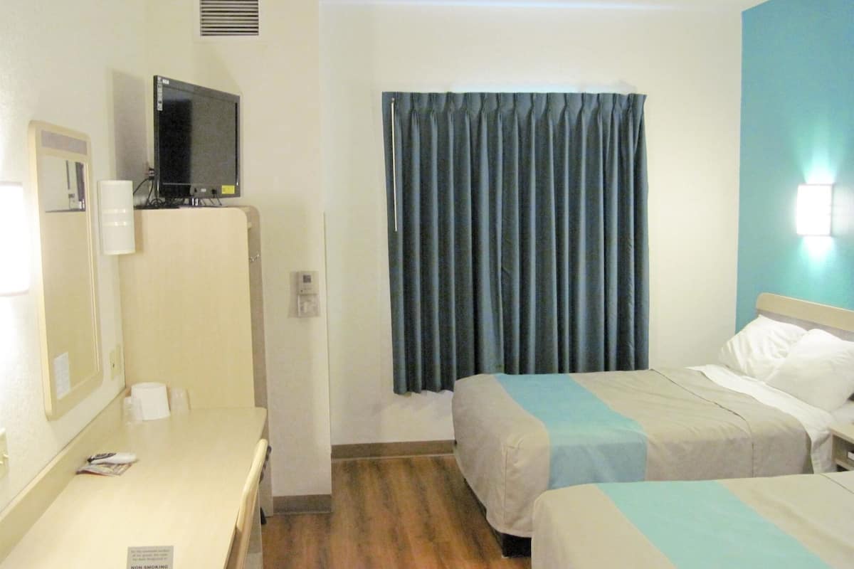 A hotel room with two beds, a desk, a TV, and a window with curtains.
