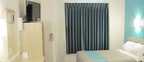 A hotel room with two beds, a desk, a TV, and a window with curtains.