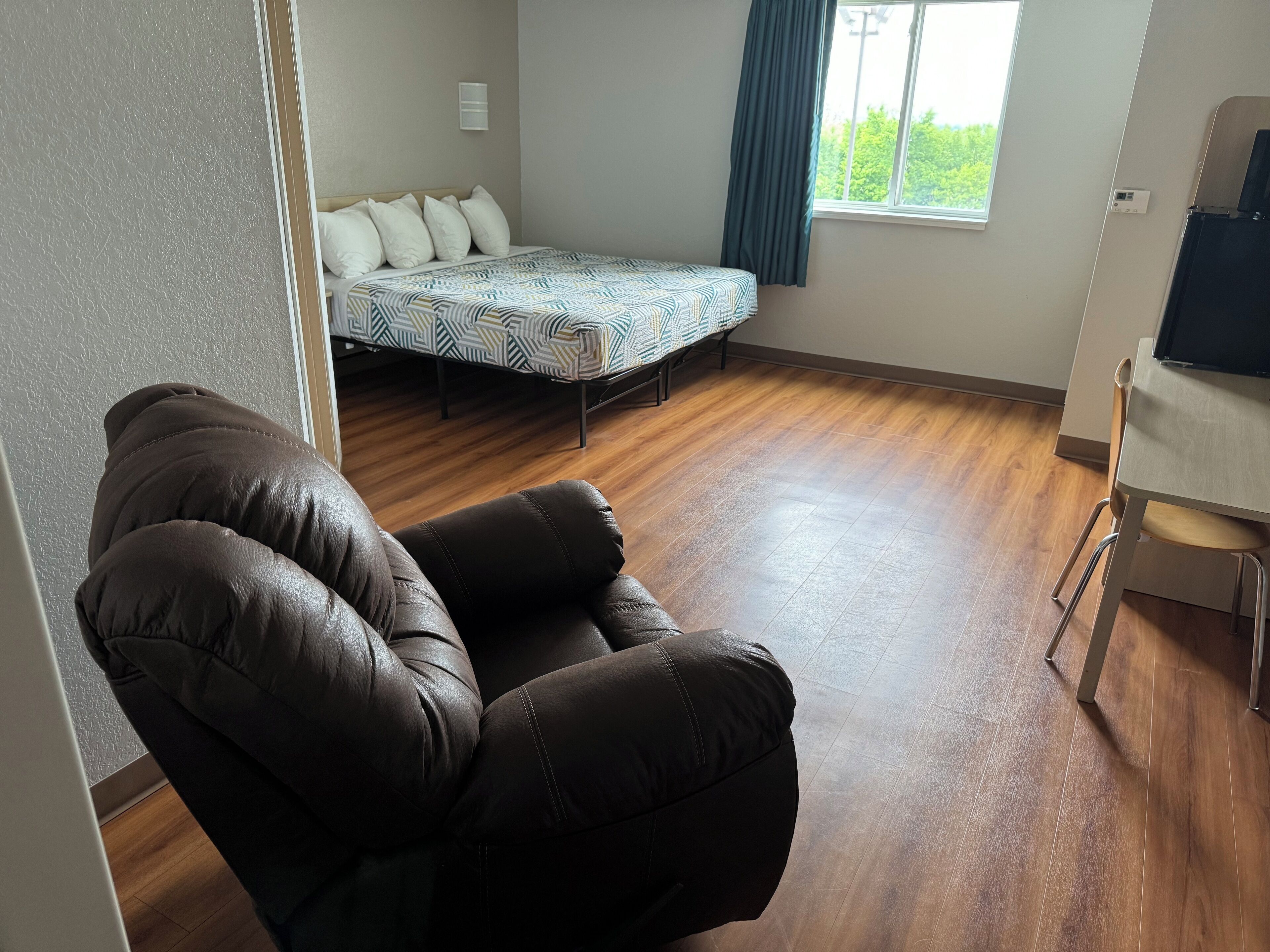 Une pièce comprenant un lit, une chaise, un bureau et une fenêtre avec des rideaux.