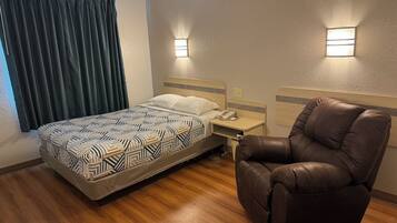 A hotel room with a bed, a nightstand, a brown leather chair, and two wall-mounted lights.