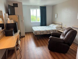 Habitación de hotel con cama, escritorio con computadora, silla y televisor sobre un soporte.