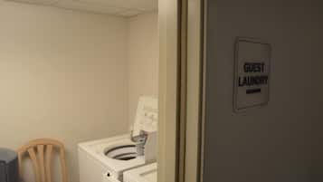 Zona de lavandería para huéspedes con lavadora y secadora, una silla y un cartel que indica la ubicación.