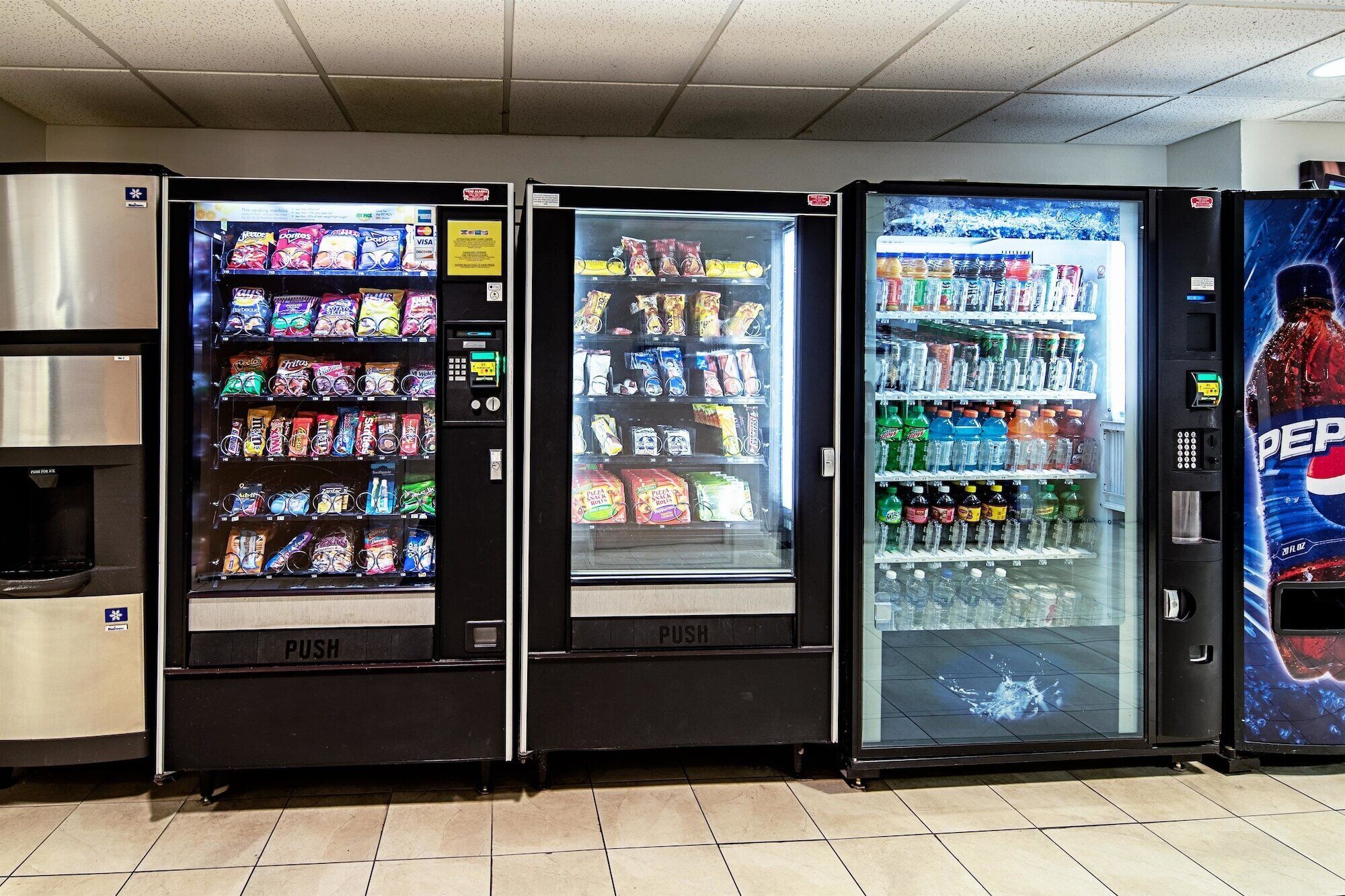 Three beverage vending machines with a variety of snacks and drinks, including chips, soda, and bottled water.