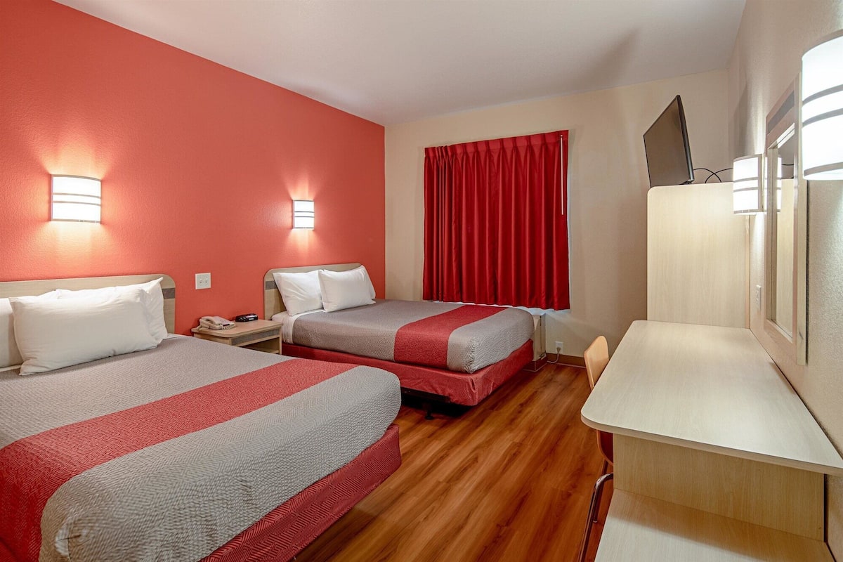 A hotel room with two beds, a desk, and a TV.