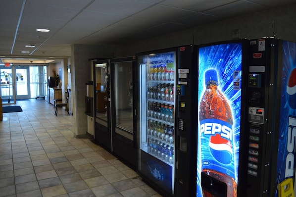 Una fila de máquinas expendedoras con publicidad de Pepsi, situadas en un pasillo con suelo de baldosas y una puerta al fondo.
