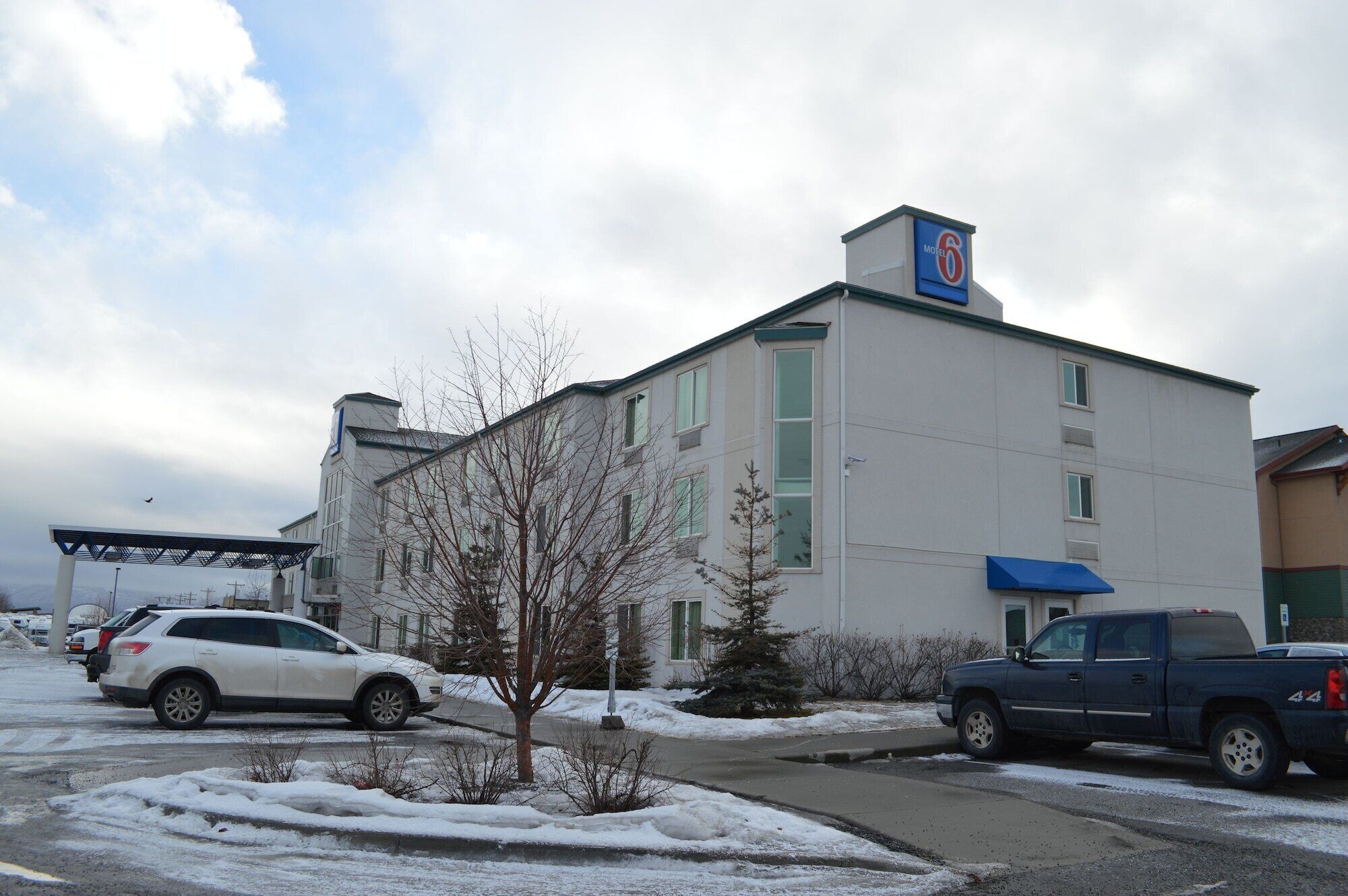 A motel with a large sign on the roof, a parking lot with several cars, and a snow-covered ground.