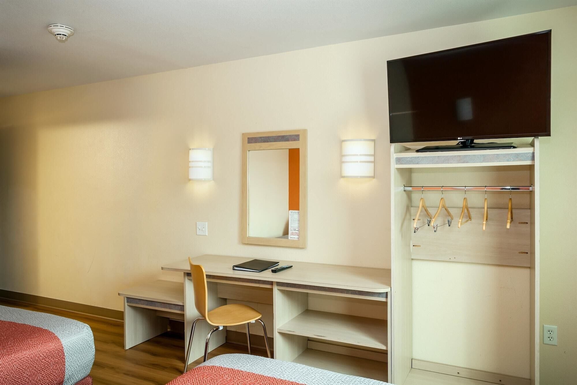 Hotellihuone, jossa on sänky, työpöytä tuolilla, televisio ja vaatekaappi henkareineen.