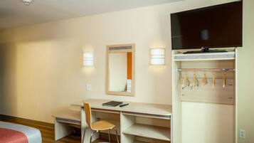A hotel room with a bed, a desk with a chair, a television, and a wardrobe with hangers.