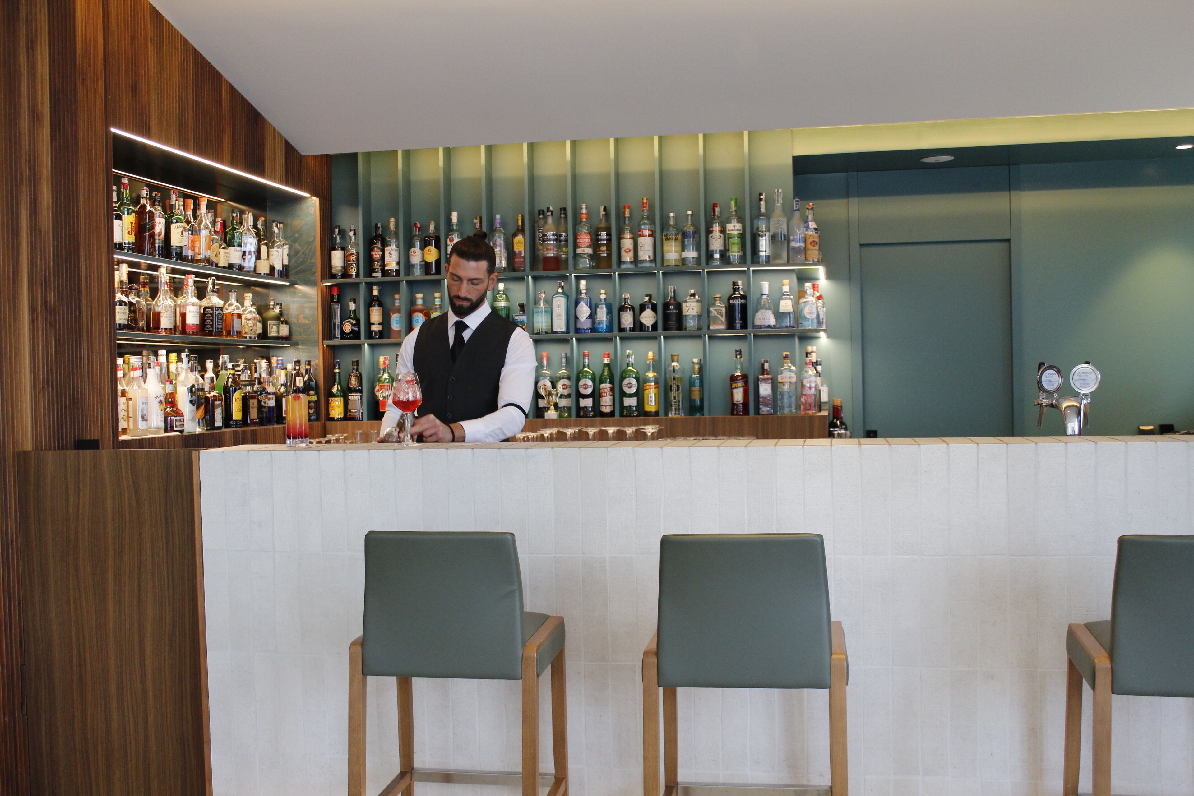A bar area with a bartender, shelves of liquor bottles, and bar stools.