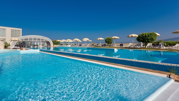 A large outdoor swimming pool with lounge chairs and umbrellas, surrounded by buildings and a clear sky. - Towers Hotel Stabiae Sorrento Coast (Castellammare di Stabia)