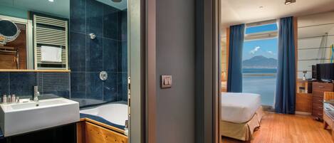 A modern hotel room with a large bed, a bathroom with a bathtub, and a view of the sea.