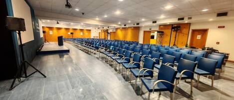 A conference room with rows of blue chairs, a stage, and a projector.