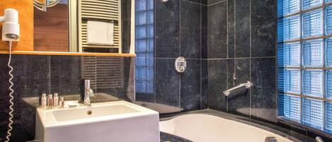 A modern bathroom with a large bathtub, a white sink, a mirror, and a towel rack.