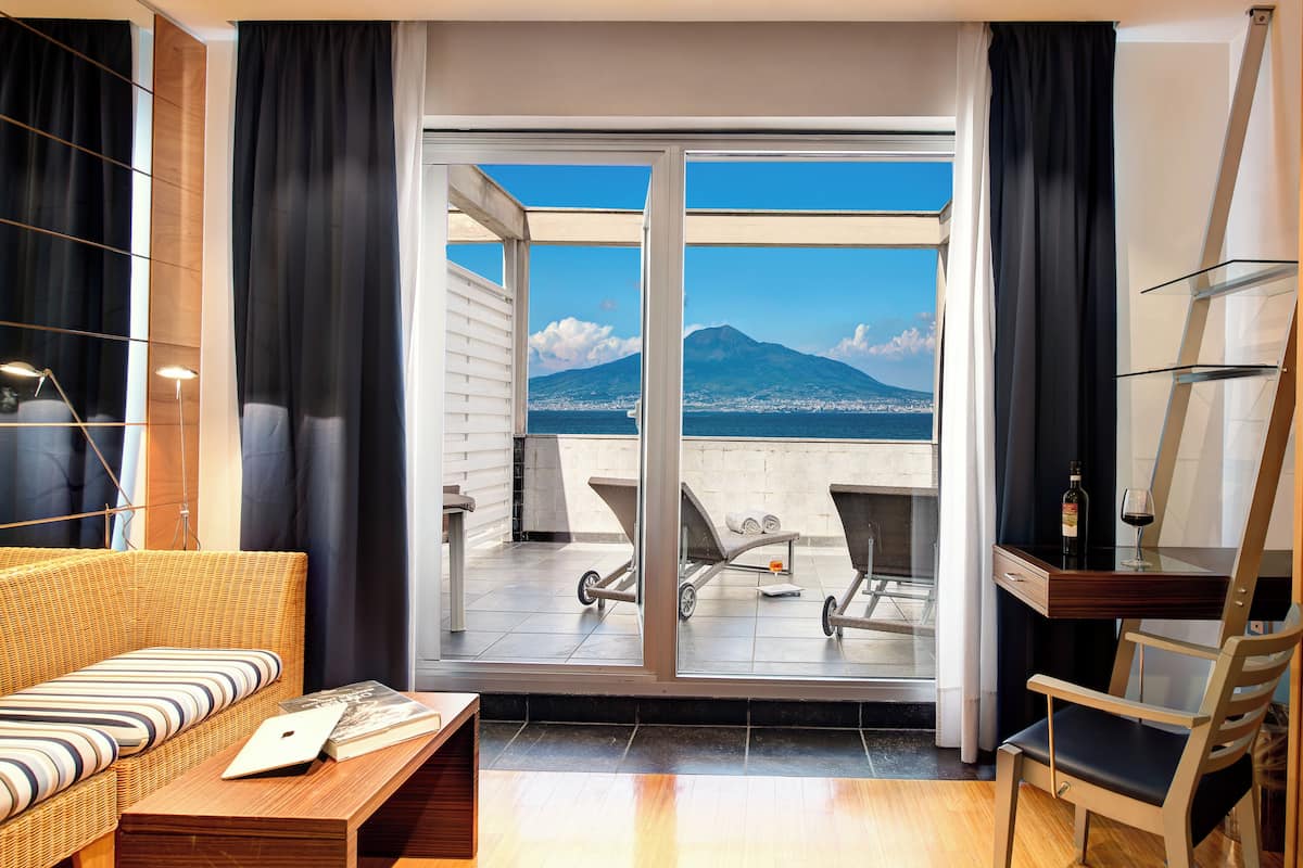 Ein modernes Zimmer mit Balkon, einem Korbsessel, einem Holztisch und einem Glastisch mit Flasche und Glas.