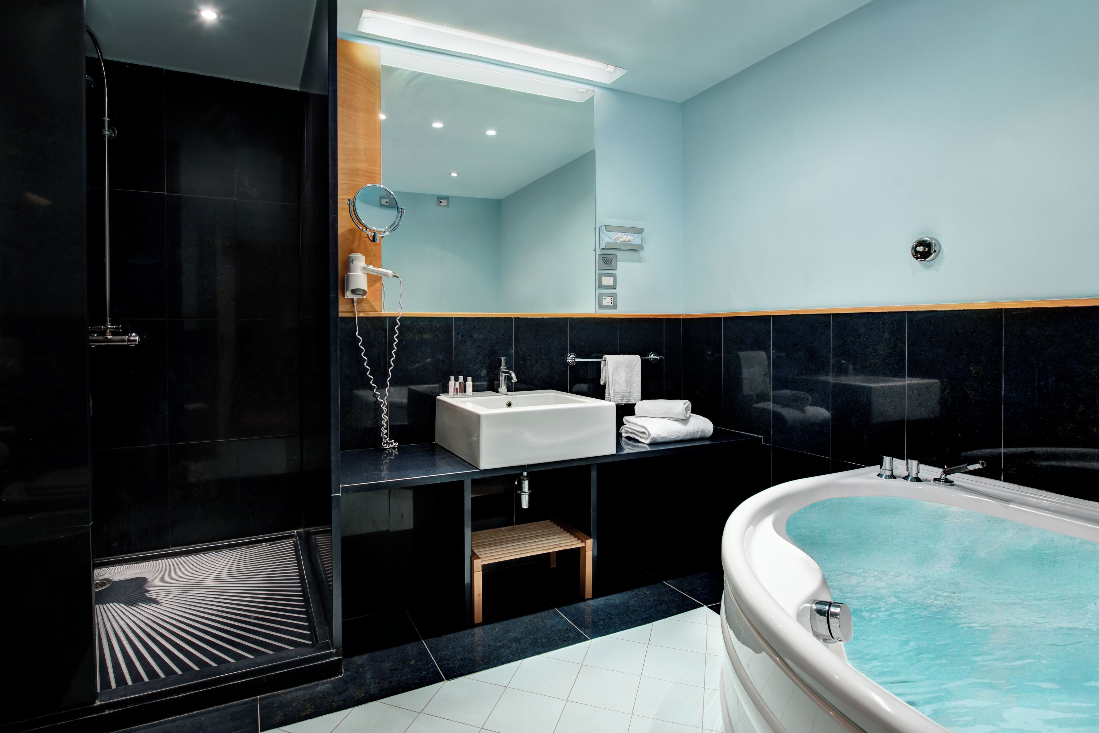 A modern bathroom with a large bathtub, a shower area, a sink, and a mirror.
