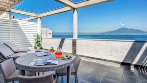 A terrace with wicker furniture, a table with a magazine, a pitcher of orange drink, and a view of the sea and a mountain. - Towers Hotel Stabiae Sorrento Coast (Castellammare di Stabia)