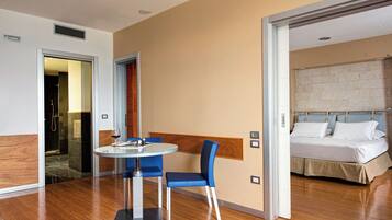 Una camera d'albergo con un letto, un tavolo rotondo con sedie, pavimento in legno e bagno visibile attraverso una porta aperta.