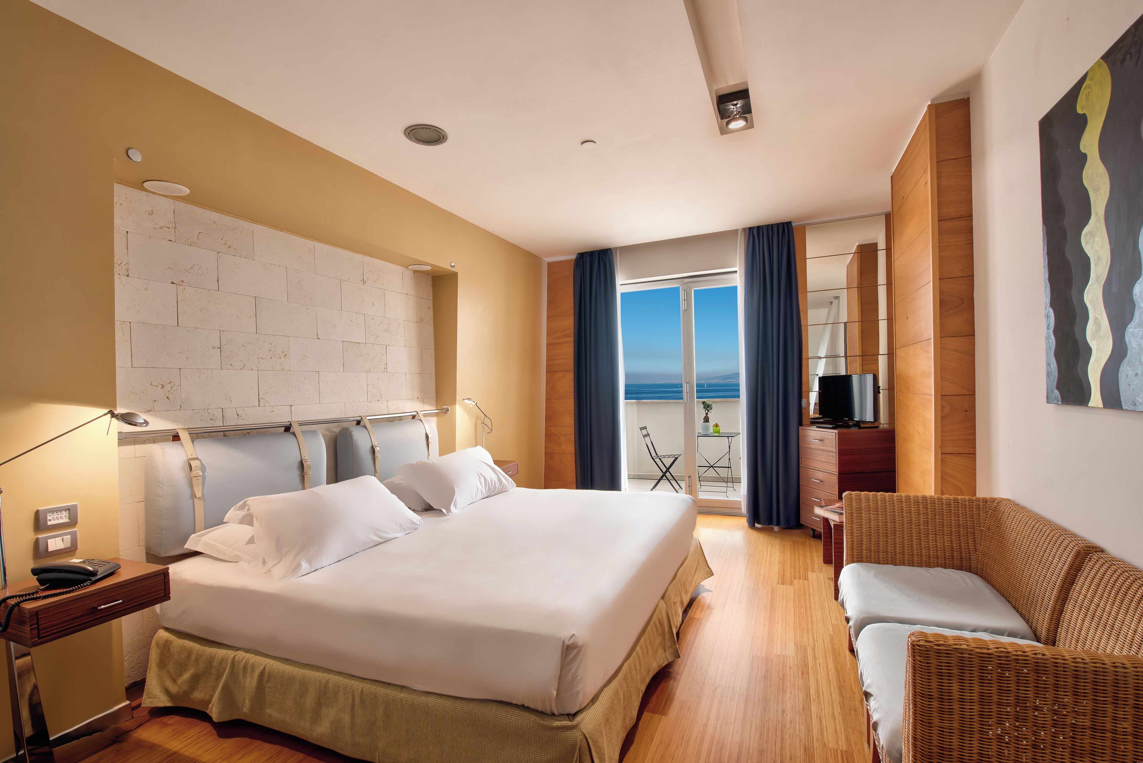 Ein Hotelzimmer mit einem großen Bett, einem Schreibtisch mit Lampe, einem Fernseher und Blick ins Freie.