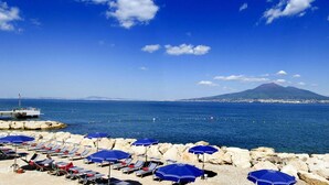 A beach with sun loungers and umbrellas, a rocky shoreline, and a mountain in the background. - Towers Hotel Stabiae Sorrento Coast (Castellammare di Stabia)