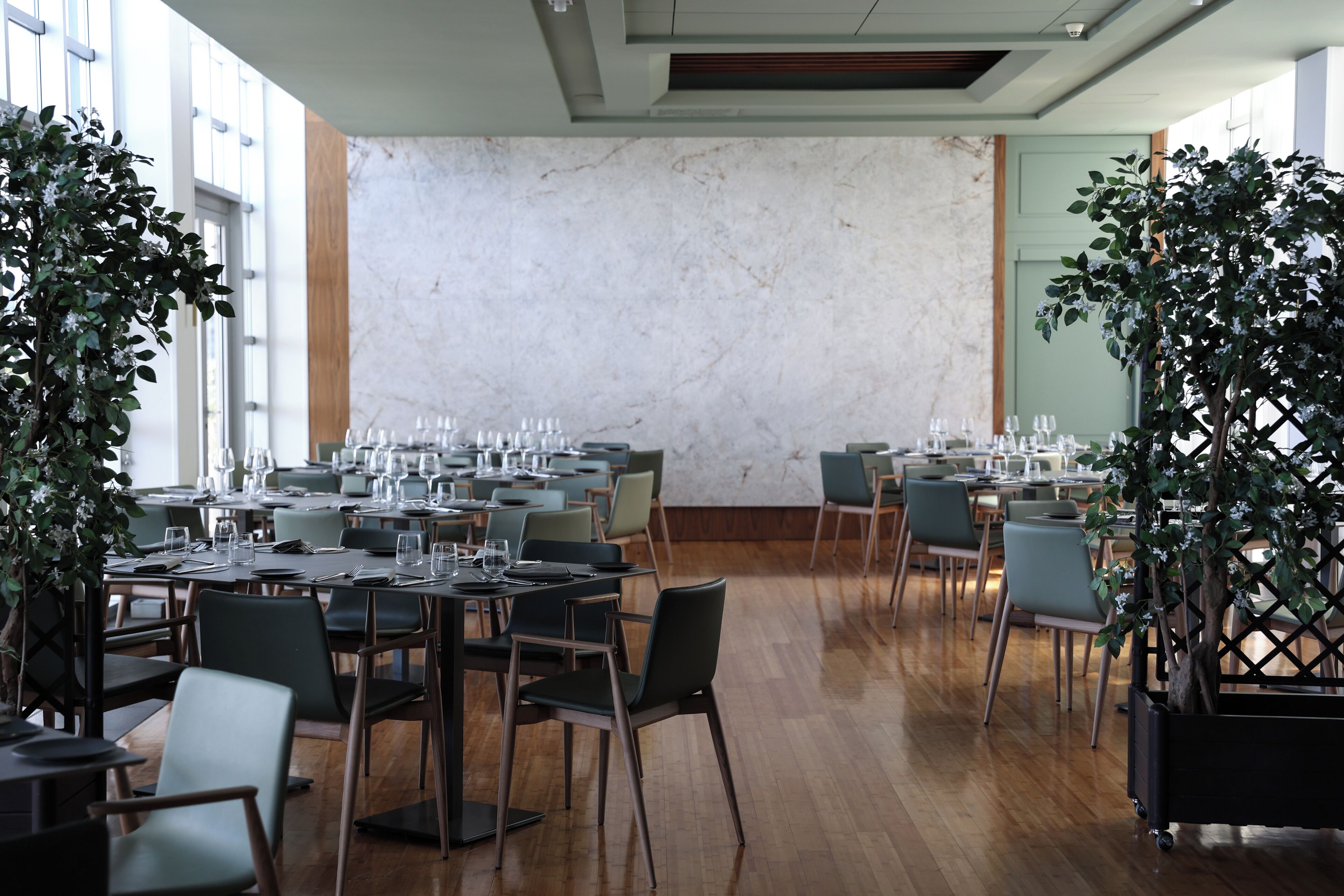 A dining area with tables set for service, large windows, and a marble wall.