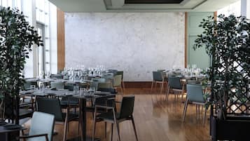 Zona de menjador amb taules preparades per al servei, grans finestres i una paret de marbre.