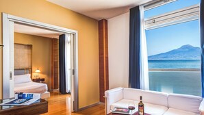 A hotel room with a bed, a sofa, a table with a bottle and glass, and a large window with a view of a mountain and sea. - Towers Hotel Stabiae Sorrento Coast (Castellammare di Stabia)