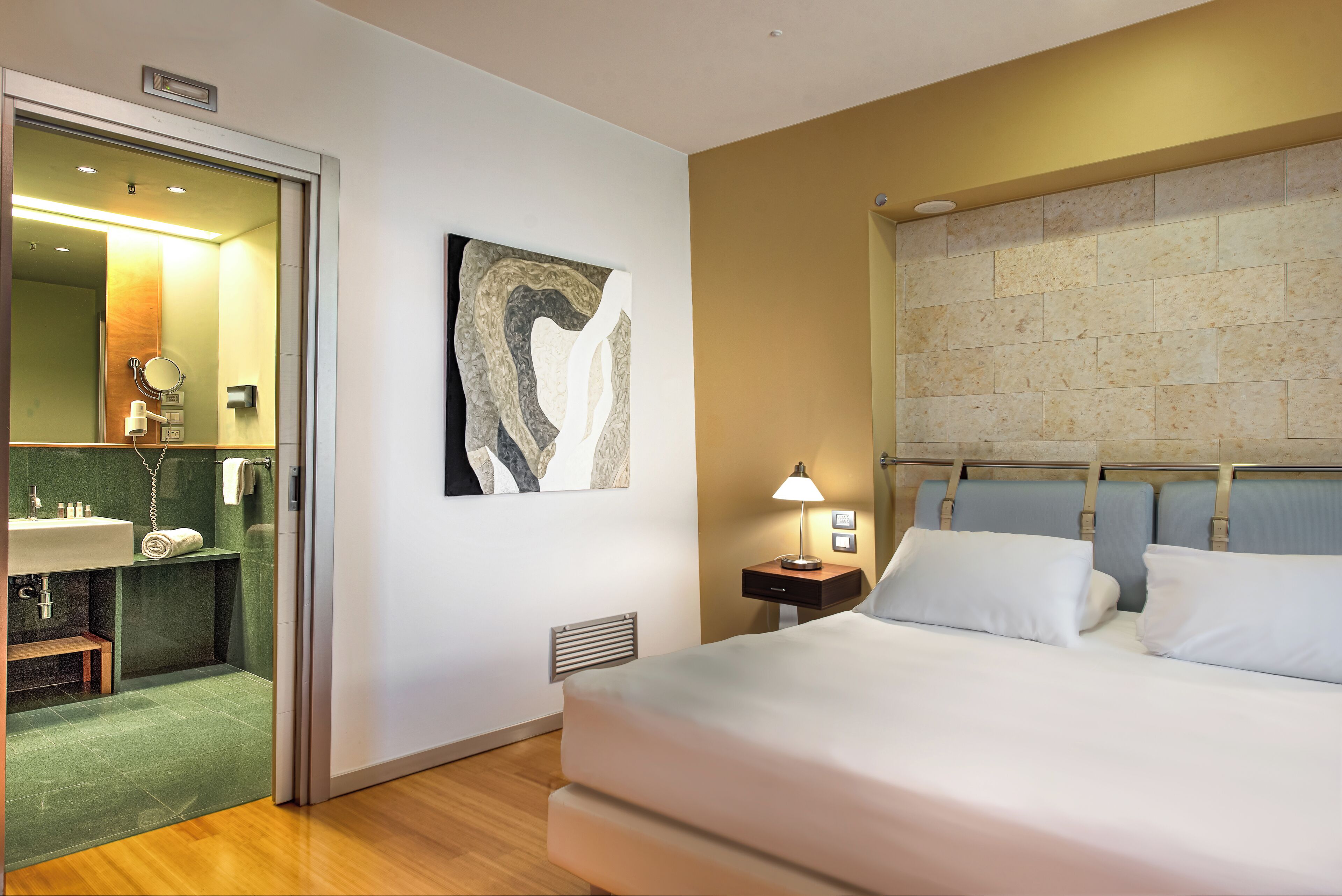 Une chambre d’hôtel comprenant un lit, une table de chevet avec une lampe, une salle de bain avec un lavabo et un miroir.