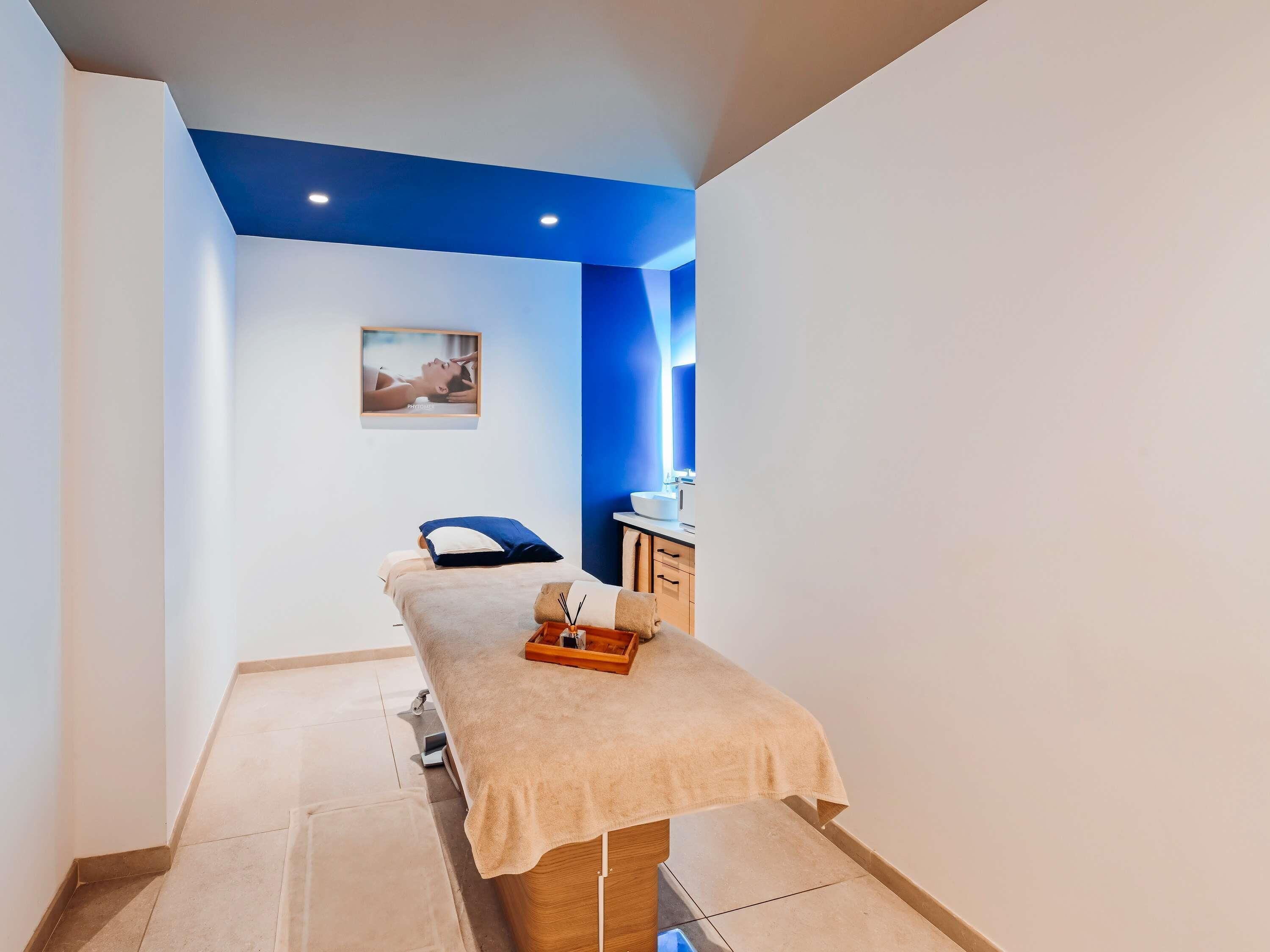 A treatment room with a massage table, a small cabinet, and a framed picture on the wall.