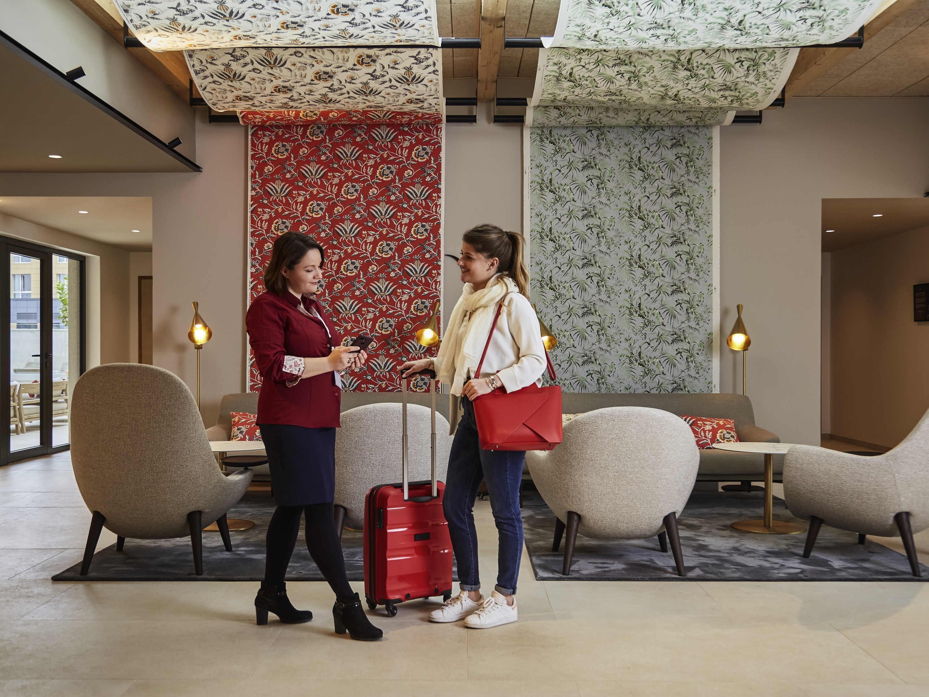 A lobby with a seating area, a red suitcase, and a person holding a phone.