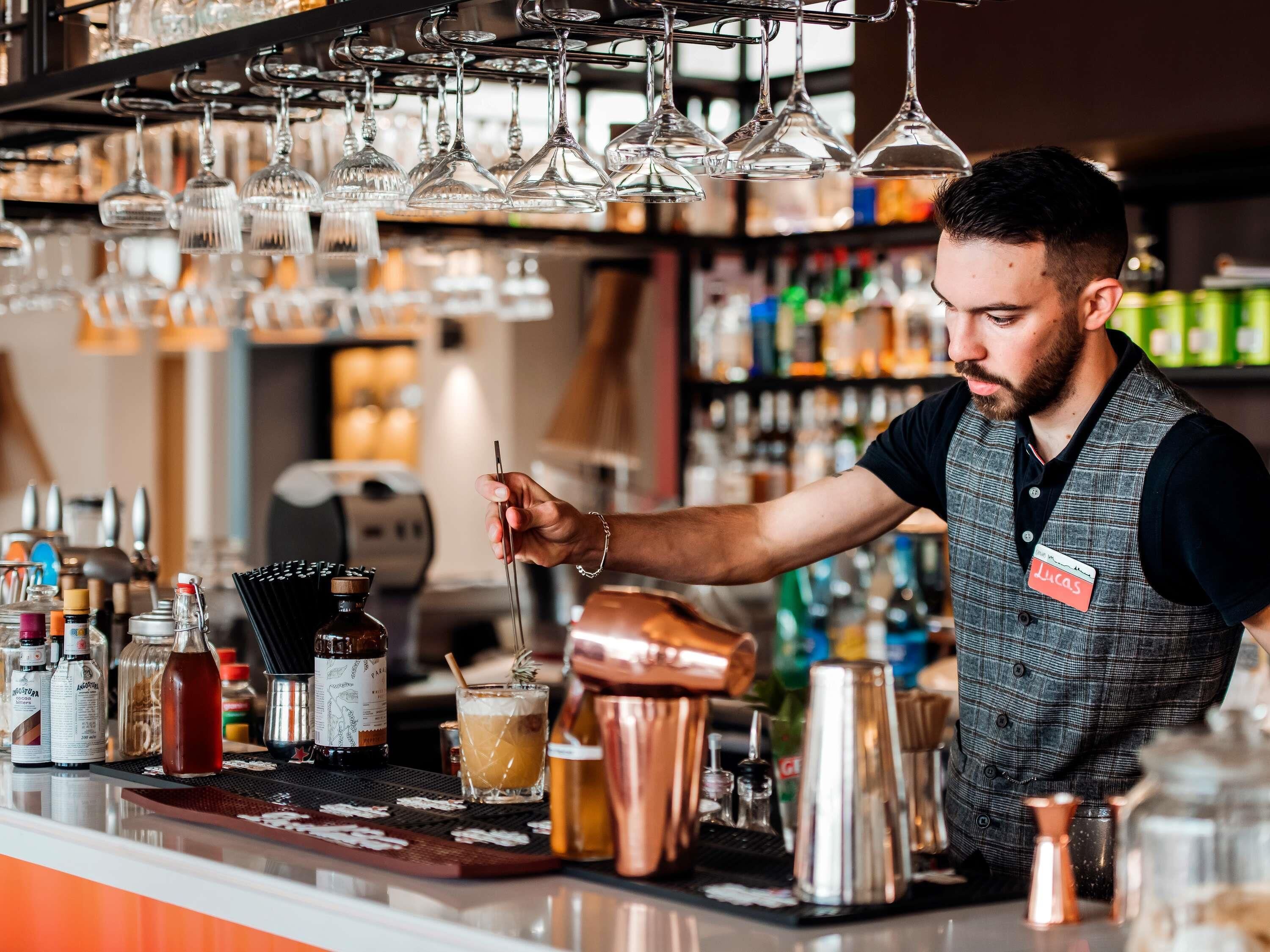 Un barista dietro al bancone di un bar, circondato da diverse bottiglie e un drink.