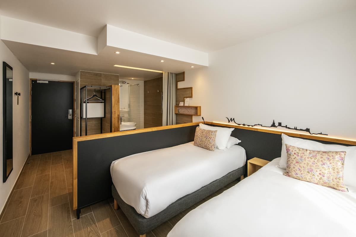 Ein Hotelzimmer mit zwei Betten, einem Badezimmer und einem Spiegel.