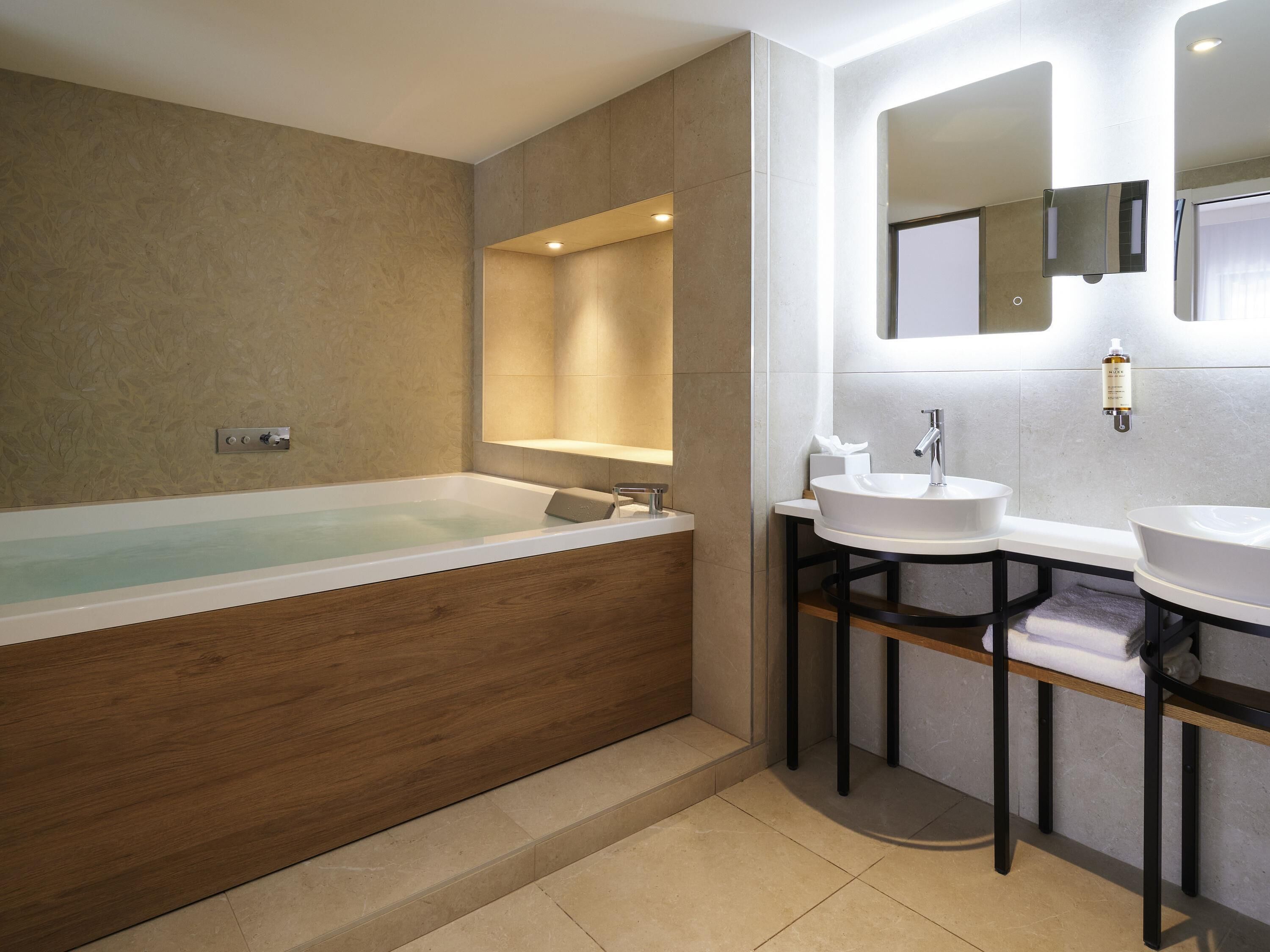 A modern bathroom with a bathtub, two sinks, and a mirror.