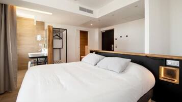 Una habitación de hotel moderna con una cama grande, una mesita de noche, un espejo y una zona de baño pequeña.