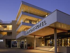 A modern hotel with a prominent sign, multiple balconies, and a covered entrance area.