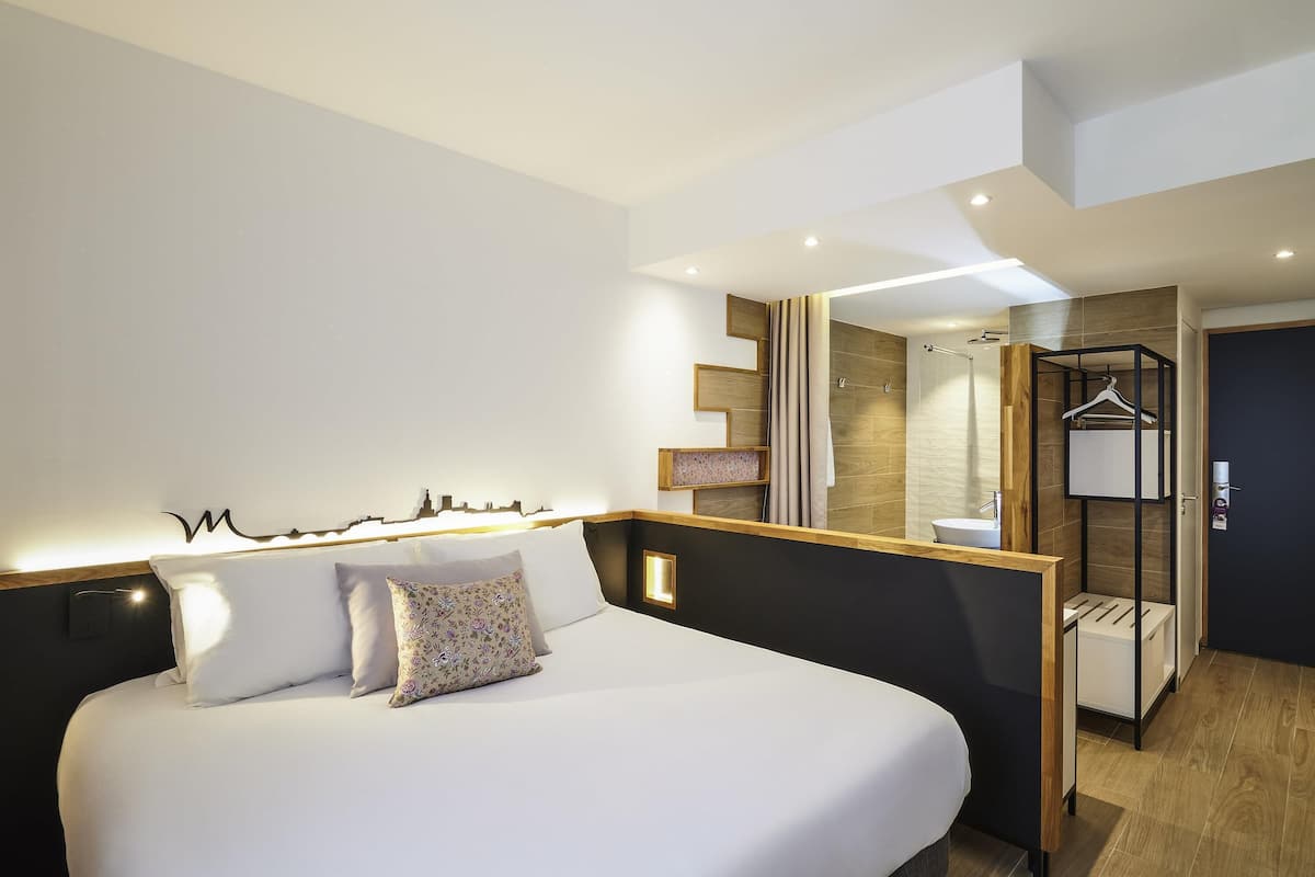 Ein modernes Hotelzimmer mit einem großen Bett, einem Badezimmer mit Dusche und einem Kleiderhaken.