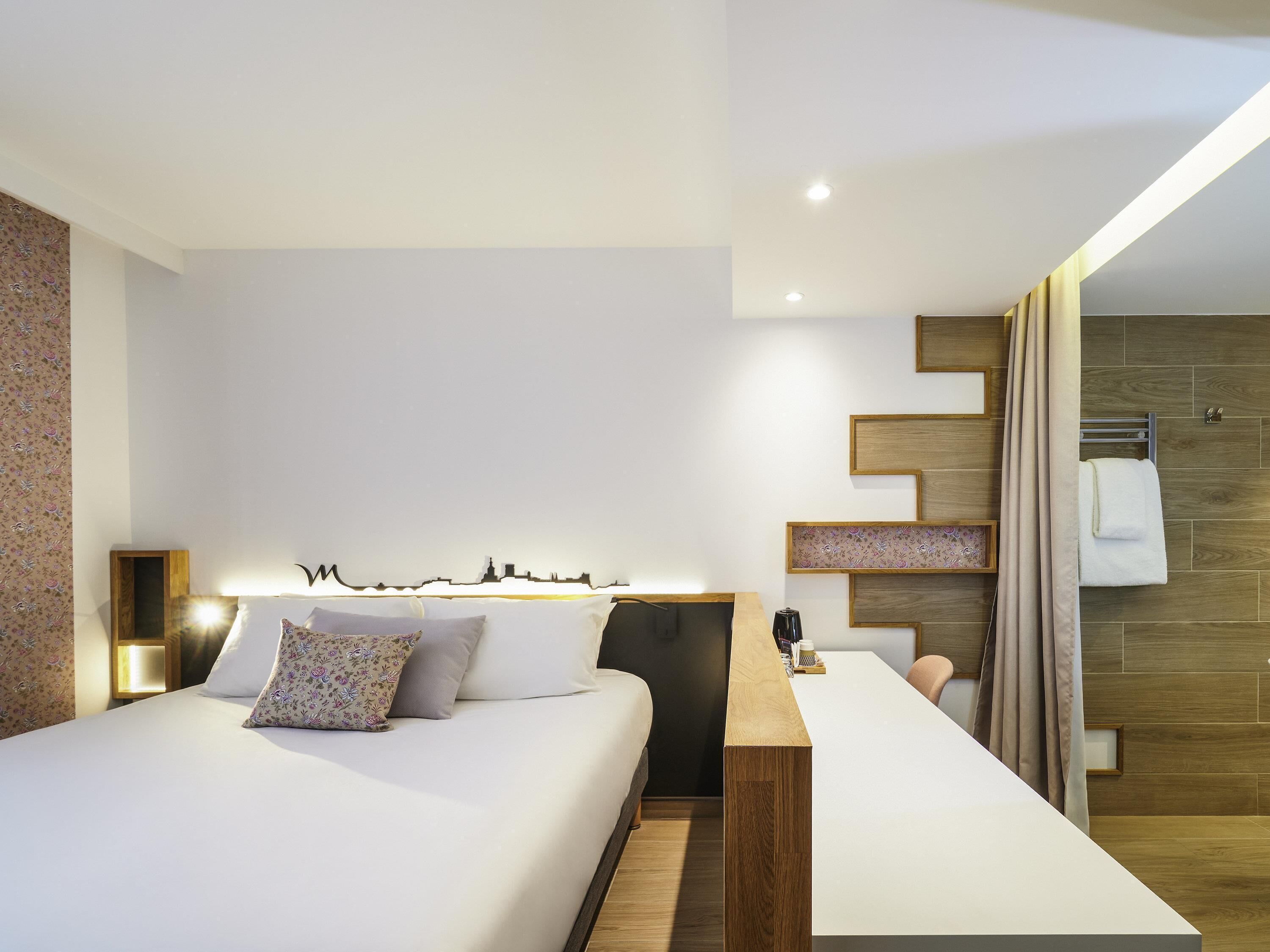 Ein modernes Hotelzimmer mit Bett, Nachttisch und Blick ins Badezimmer.