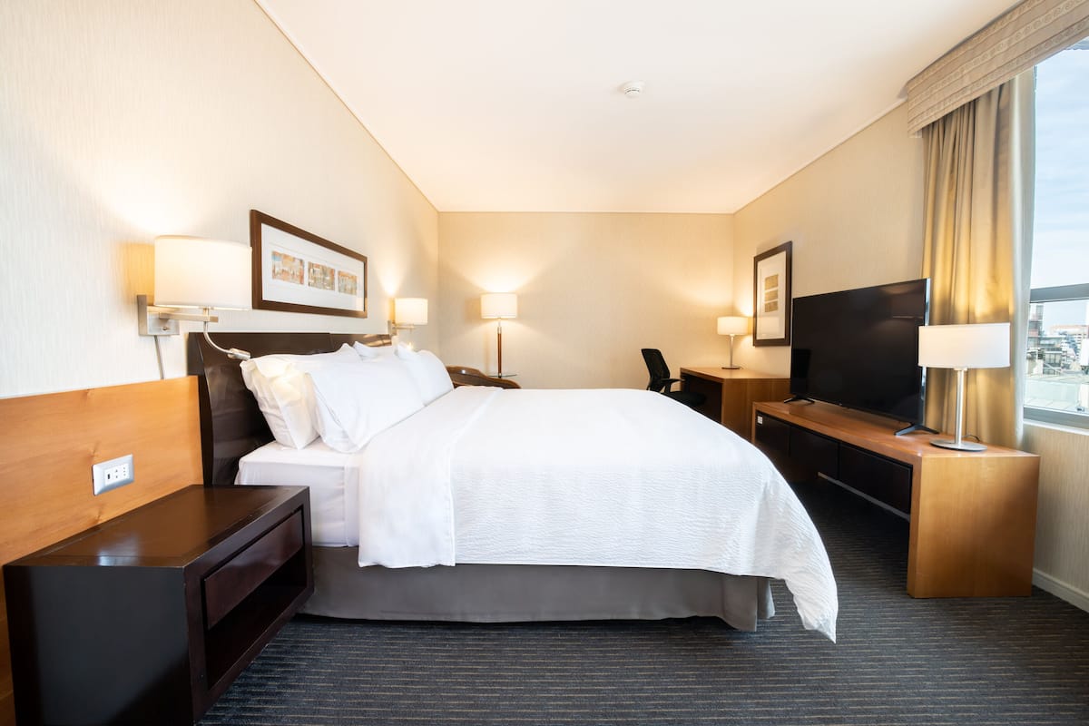 A hotel room with a large bed, bedside tables, a TV, and a desk with a chair.