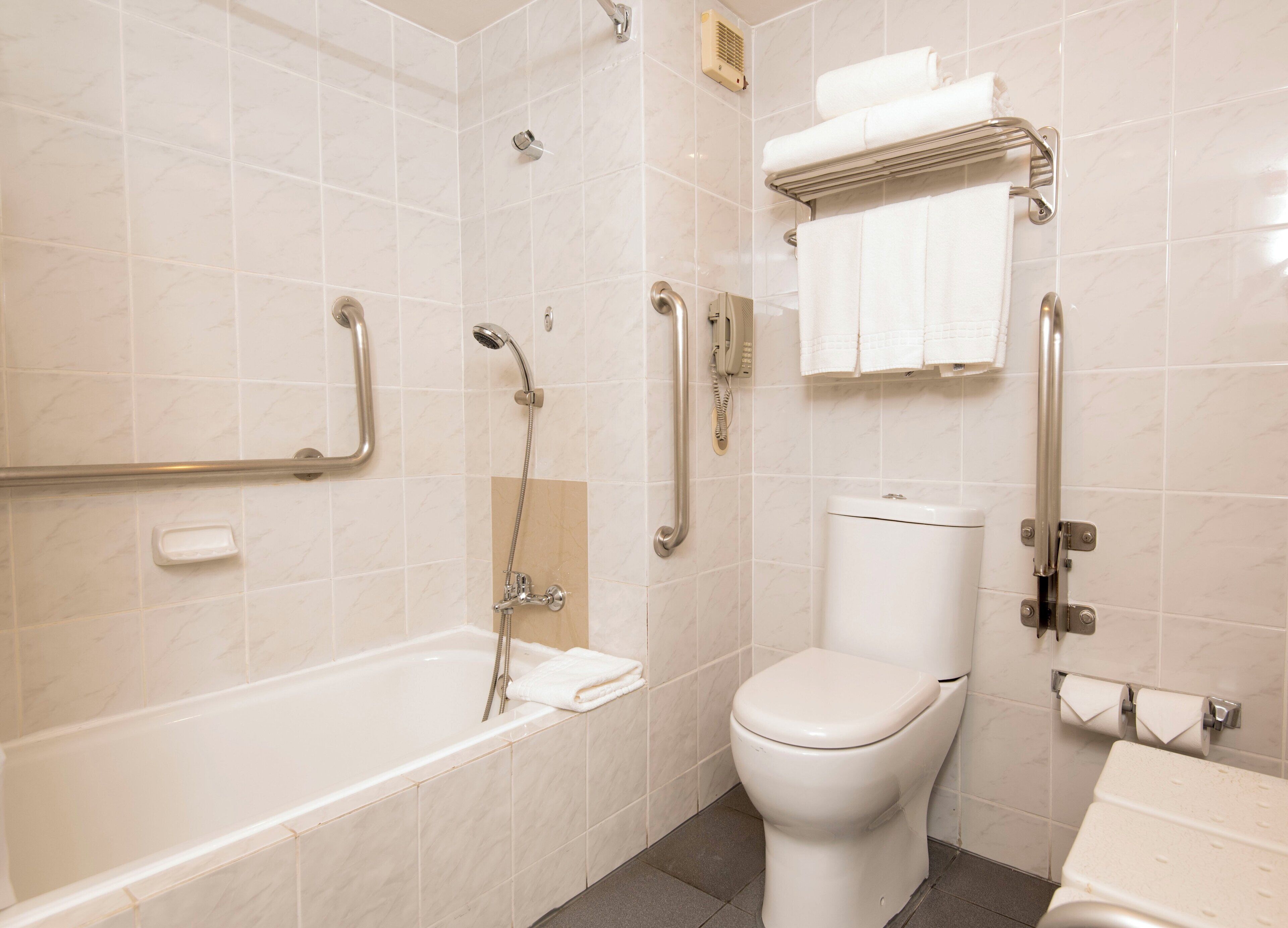 A bathroom with a bathtub, toilet, and handrails.