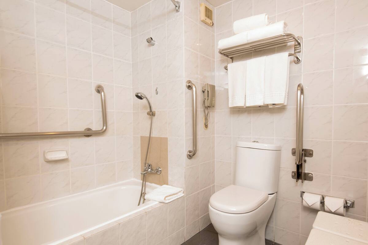 Un baño con bañera, inodoro y barras de apoyo.