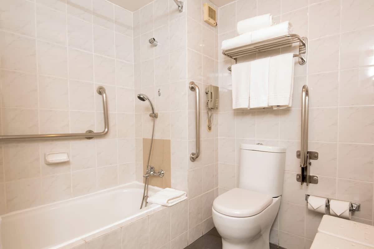 A bathroom with a bathtub, toilet, and handrails.