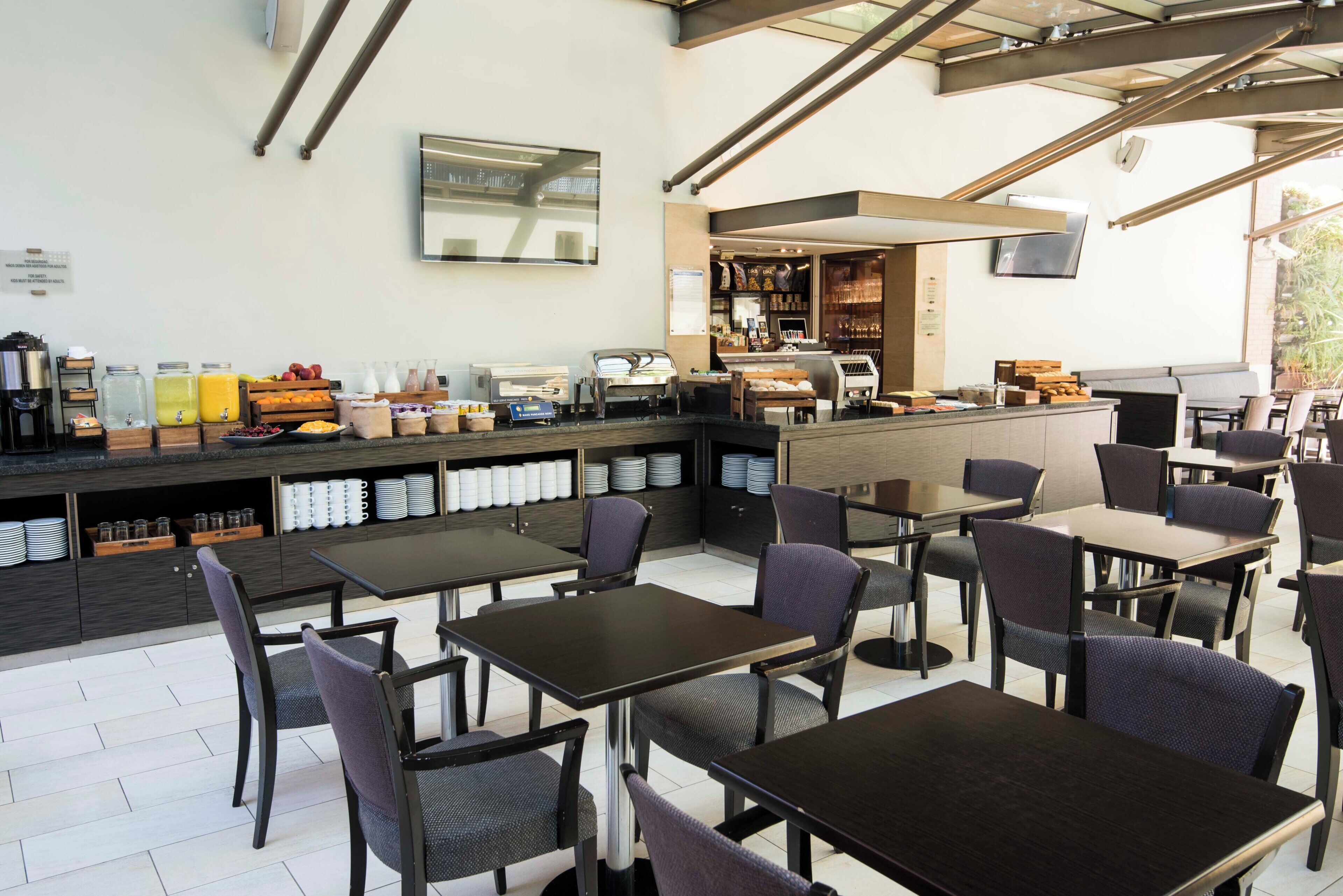 Un café con terraza, una barra con distintos productos alimenticios y un amplio ventanal.