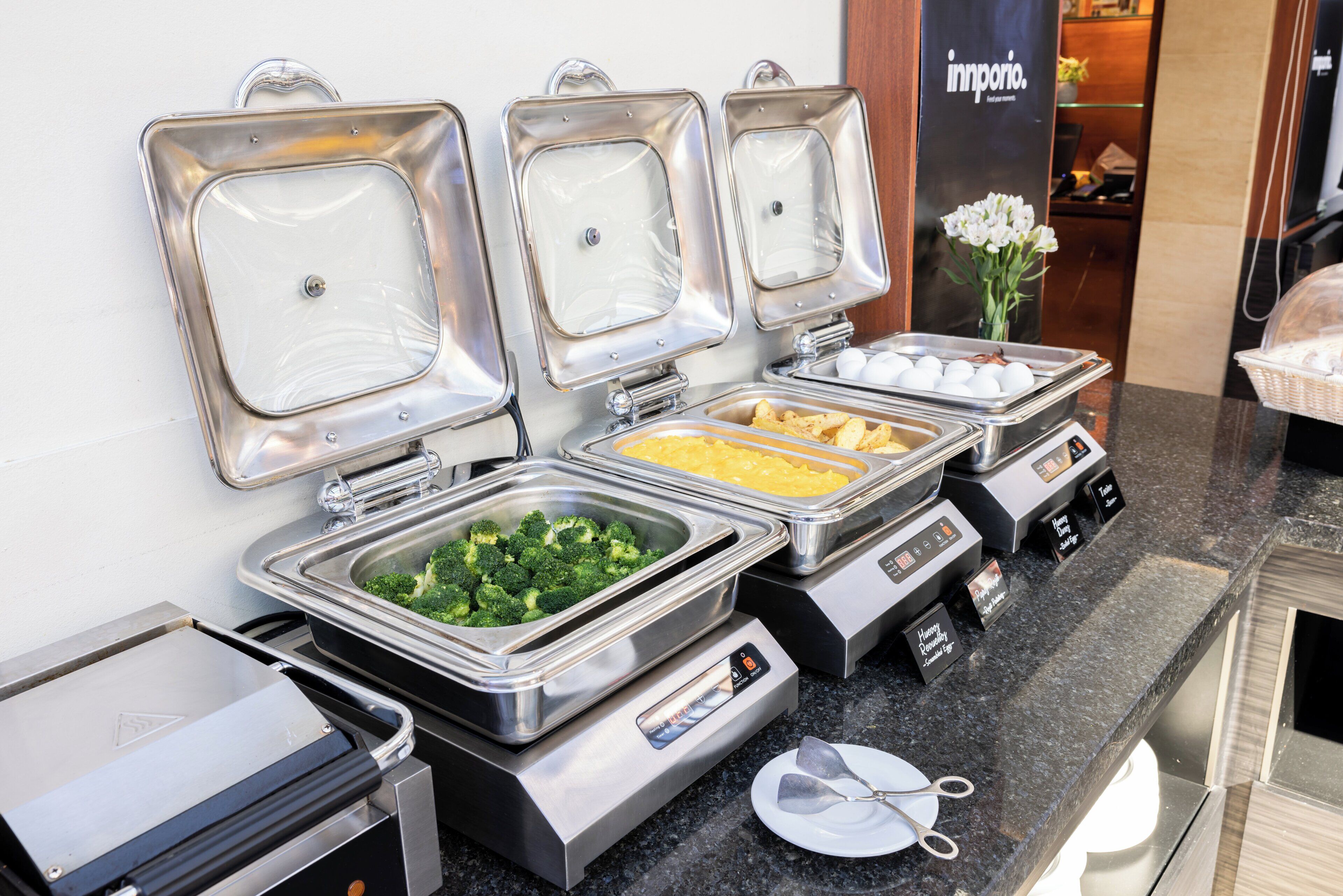 A buffet setup with various food items in metal containers, a digital scale, and a small plate with utensils.