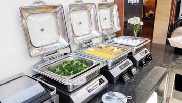 A buffet setup with various food items in metal containers, a digital scale, and a small plate with utensils.