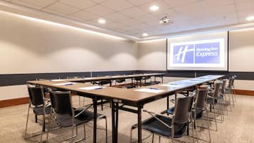 Une salle de conférence avec une longue table, des chaises, un écran de projection et un sol recouvert de moquette.