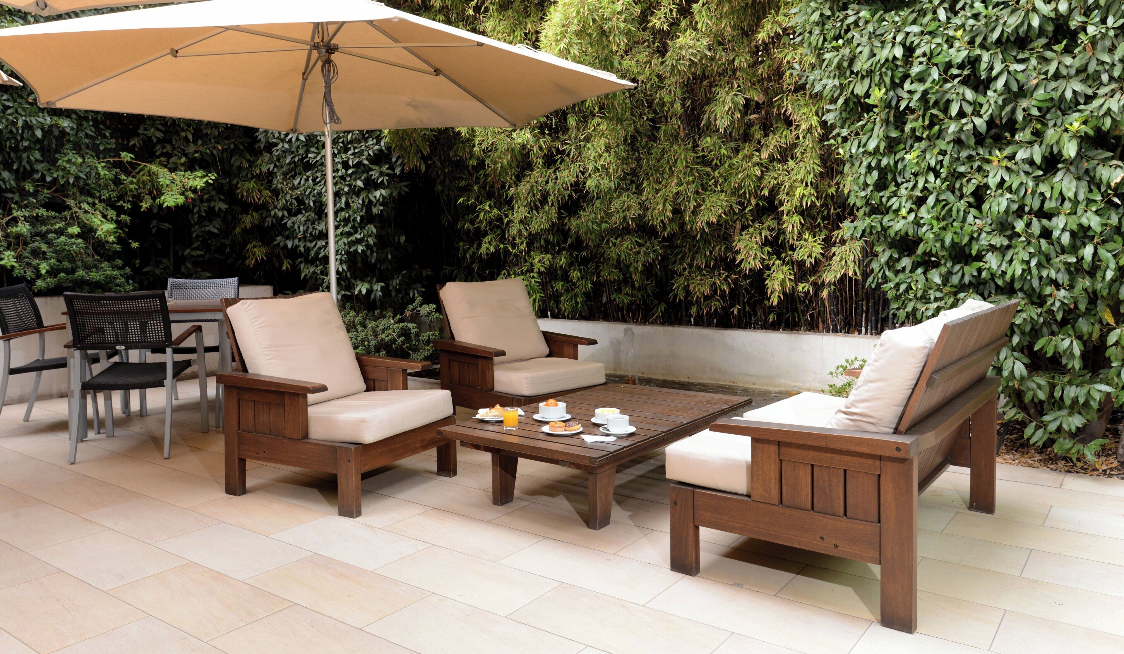 Un espacio de estar al aire libre con mobiliario de madera y una mesa lista para una comida, rodeado por un muro verde exuberante.